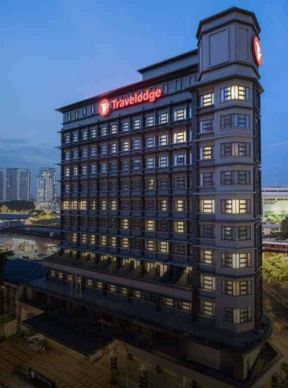 Exterior view of Travelodge hotel near SOGO KL at dusk, featuring a modern high-rise design with city lights in the background.